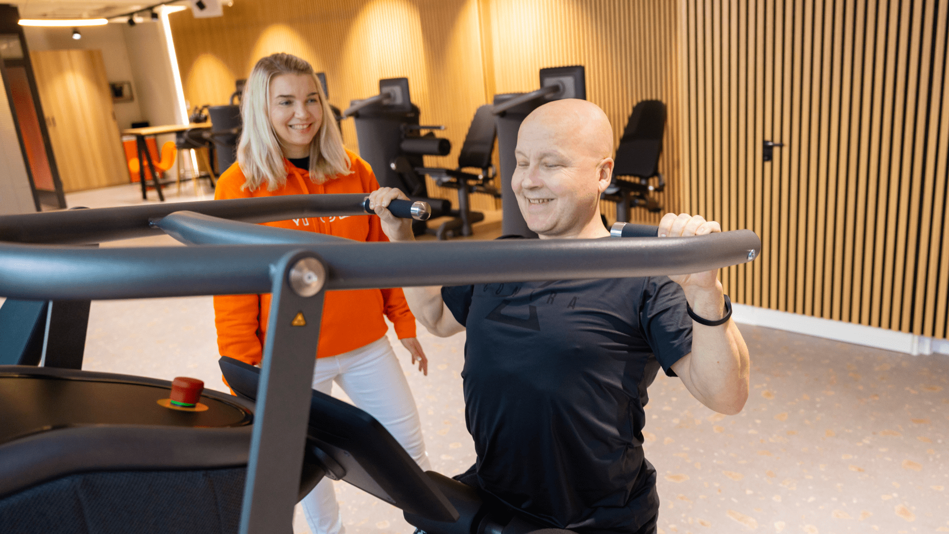 MyHubin hosti ja asiakas tekemässä voimatestejä, kuvassa nainen vieressä, kun mies tekee laitteella testiä 