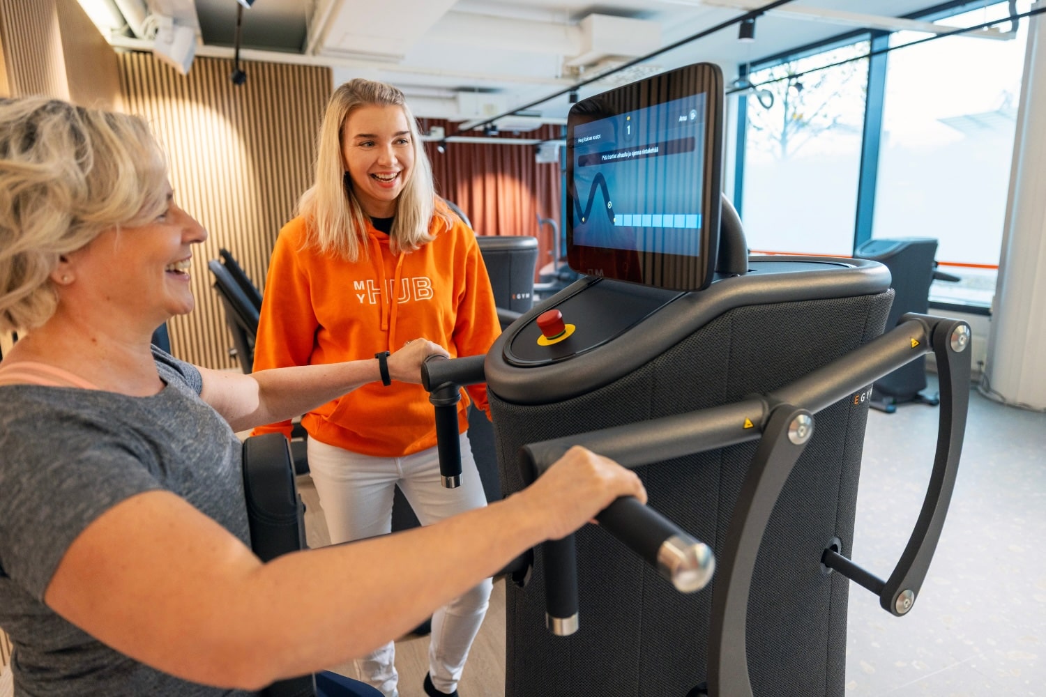 Nainen tekee MyHubilla egym-treeniä, MyHubin hosti seuraa vieressä.
